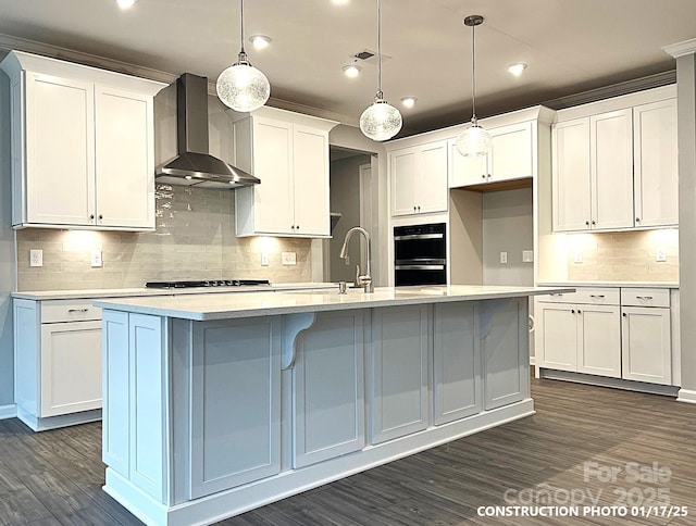 kitchen featuring hanging light fixtures, a kitchen island with sink, white cabinets, and wall chimney exhaust hood