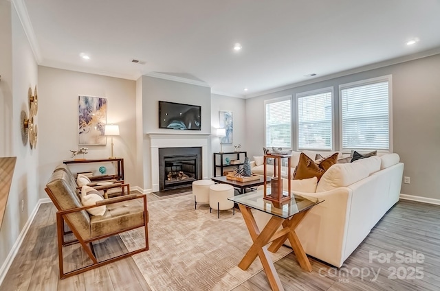 living area featuring crown molding, light wood-type flooring, a glass covered fireplace, and baseboards