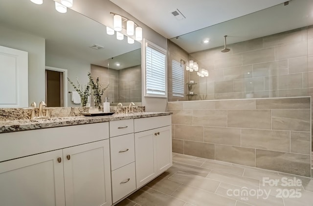 bathroom with a walk in shower, double vanity, and visible vents