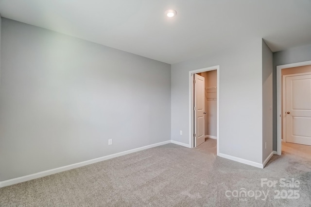 unfurnished bedroom featuring light carpet, a closet, a walk in closet, and baseboards