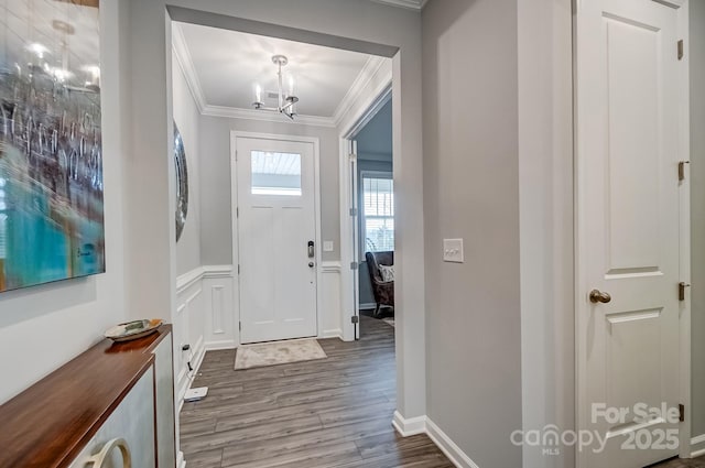 foyer with a notable chandelier, a decorative wall, wood finished floors, ornamental molding, and wainscoting