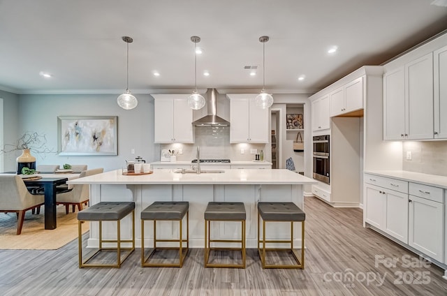 kitchen with light countertops, wall chimney range hood, a sink, and white cabinets