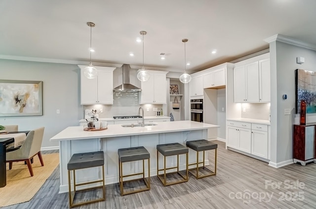 kitchen with a sink, white cabinetry, light countertops, wall chimney exhaust hood, and light wood finished floors