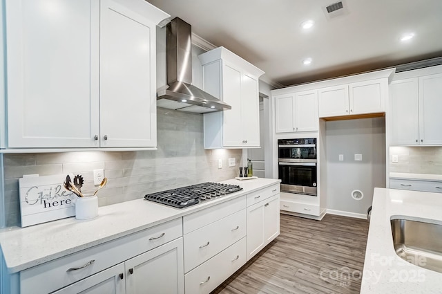 kitchen with wood finished floors, visible vents, white cabinets, wall chimney range hood, and appliances with stainless steel finishes