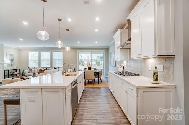 kitchen with stainless steel appliances, white cabinets, light countertops, backsplash, and an island with sink