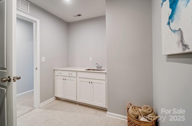 clothes washing area with visible vents, a sink, and baseboards