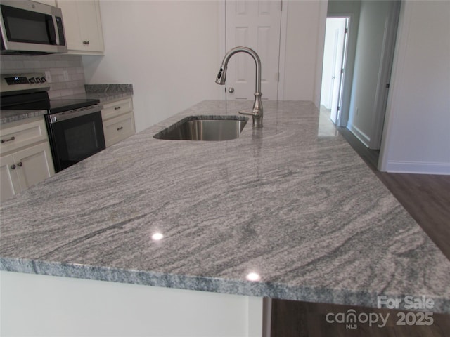 kitchen with tasteful backsplash, light stone counters, stainless steel appliances, sink, and white cabinets