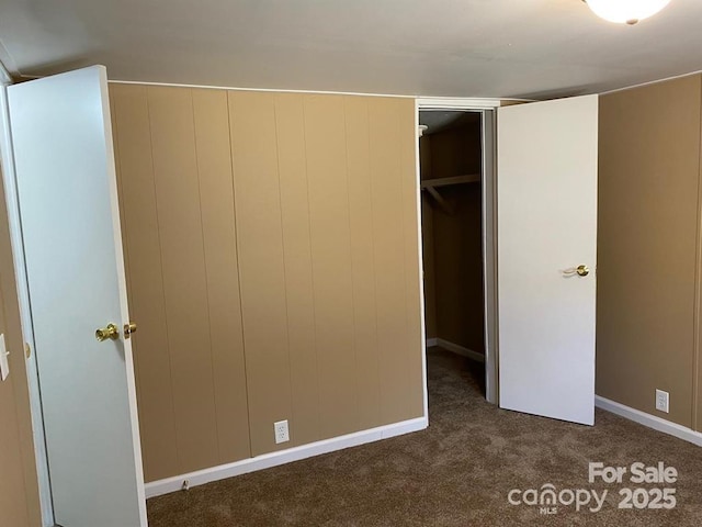 unfurnished bedroom featuring dark carpet, a spacious closet, and a closet