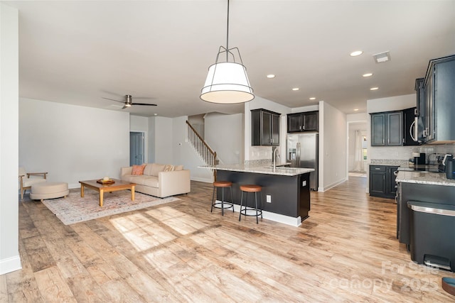 kitchen featuring light stone countertops, appliances with stainless steel finishes, ceiling fan, pendant lighting, and light hardwood / wood-style flooring