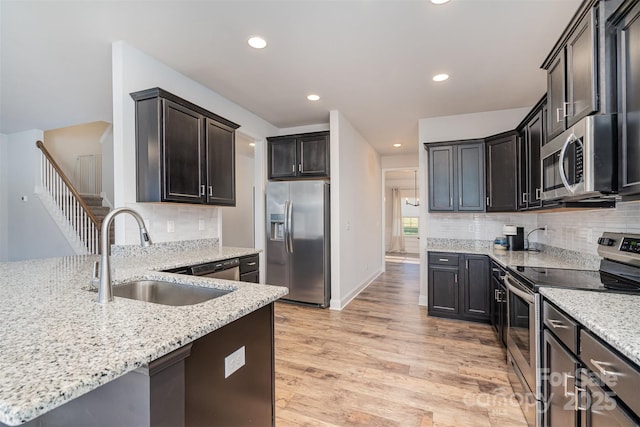 kitchen with light stone countertops, sink, stainless steel appliances, tasteful backsplash, and light hardwood / wood-style flooring