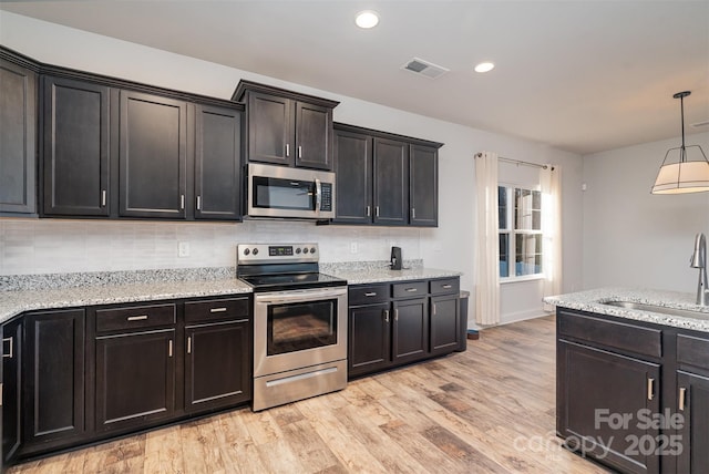 kitchen featuring sink, hanging light fixtures, stainless steel appliances, light hardwood / wood-style flooring, and backsplash