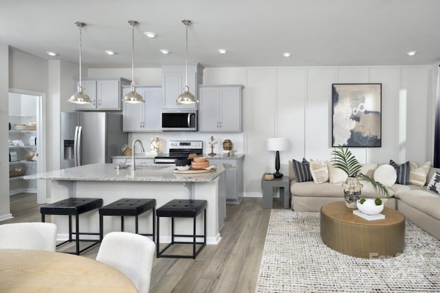 kitchen with a kitchen island with sink, light stone countertops, appliances with stainless steel finishes, decorative light fixtures, and a kitchen bar