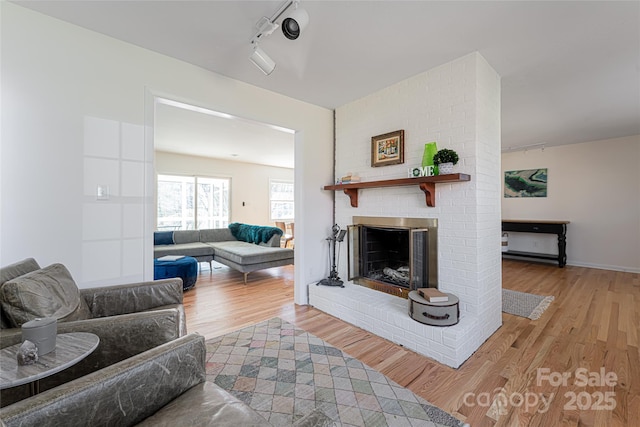 living room featuring track lighting, a brick fireplace, and light hardwood / wood-style flooring