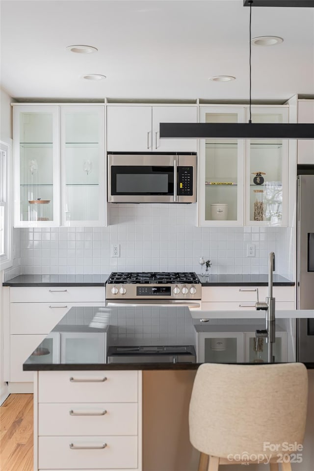 kitchen featuring tasteful backsplash, stainless steel appliances, light hardwood / wood-style floors, and white cabinets