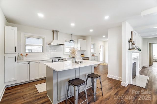 kitchen featuring white cabinets, wall chimney exhaust hood, a kitchen island, and appliances with stainless steel finishes