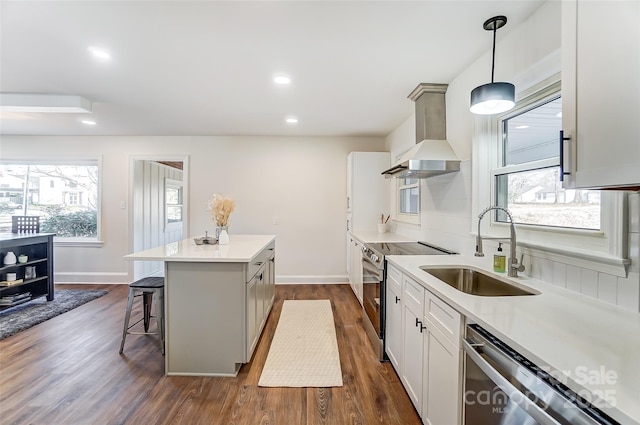 kitchen with wall chimney exhaust hood, stainless steel appliances, sink, decorative light fixtures, and white cabinets