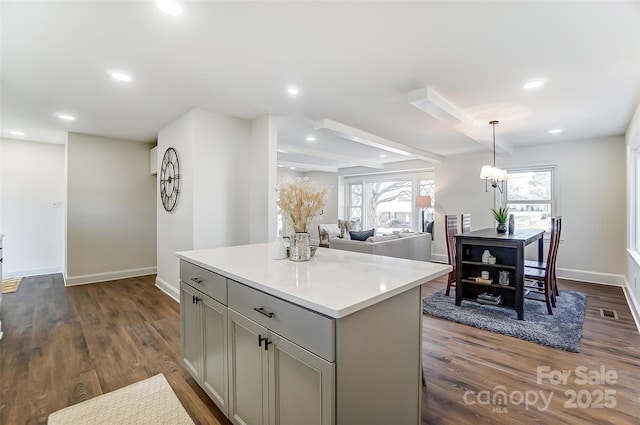 kitchen with gray cabinetry, a center island, dark hardwood / wood-style floors, beamed ceiling, and decorative light fixtures