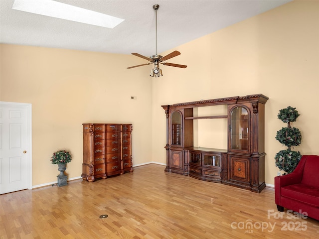 living room featuring ceiling fan, light hardwood / wood-style floors, lofted ceiling with skylight, and a textured ceiling