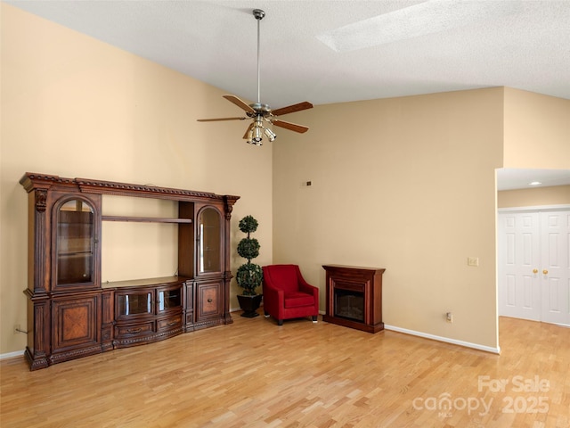 living area with ceiling fan, vaulted ceiling with skylight, and light hardwood / wood-style floors