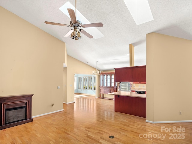 kitchen with ceiling fan with notable chandelier, light hardwood / wood-style flooring, a skylight, decorative light fixtures, and kitchen peninsula