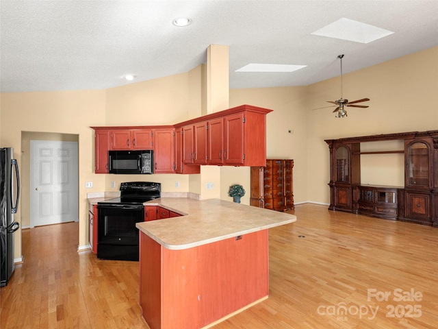 kitchen with black appliances, a skylight, ceiling fan, light hardwood / wood-style floors, and kitchen peninsula