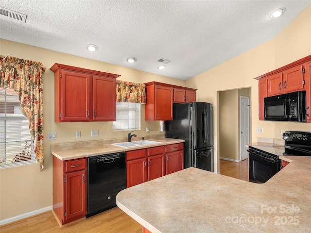 kitchen featuring sink, light hardwood / wood-style flooring, lofted ceiling, a textured ceiling, and black appliances