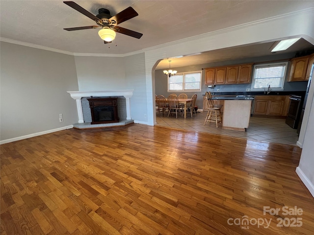 unfurnished living room with a brick fireplace, ceiling fan with notable chandelier, crown molding, sink, and hardwood / wood-style flooring