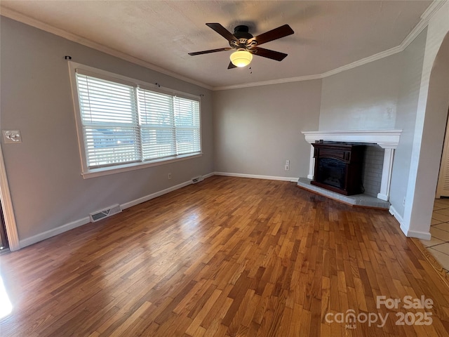 unfurnished living room featuring hardwood / wood-style floors, ceiling fan, ornamental molding, and a fireplace