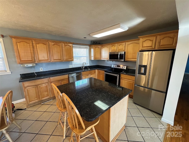 kitchen featuring sink, stainless steel appliances, a kitchen island, a textured ceiling, and light tile patterned flooring