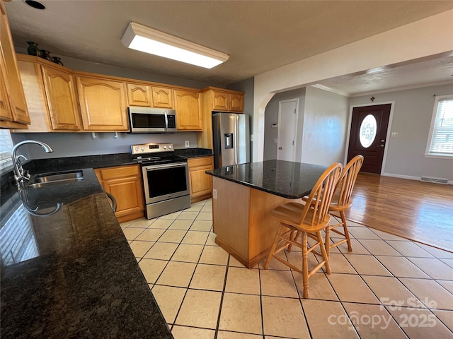 kitchen with stainless steel appliances, sink, a center island, a breakfast bar area, and light tile patterned flooring