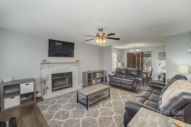 living room with a fireplace, a textured ceiling, hardwood / wood-style flooring, and ceiling fan with notable chandelier