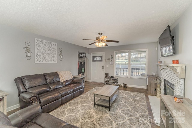 living room with ceiling fan, a fireplace, a textured ceiling, and hardwood / wood-style flooring