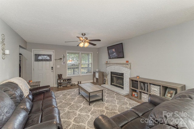 living room with a fireplace, ceiling fan, a textured ceiling, and light hardwood / wood-style flooring