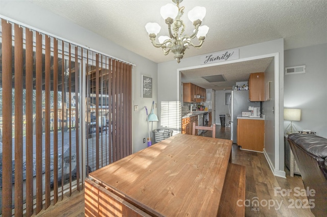 dining space featuring dark wood-type flooring, a textured ceiling, and an inviting chandelier