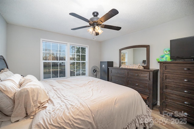 bedroom featuring ceiling fan, light hardwood / wood-style floors, and a textured ceiling