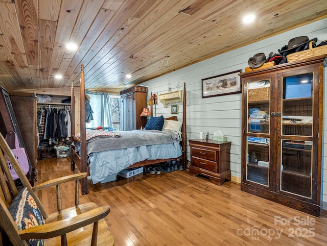 bedroom featuring wood walls, light wood-type flooring, wooden ceiling, and a closet