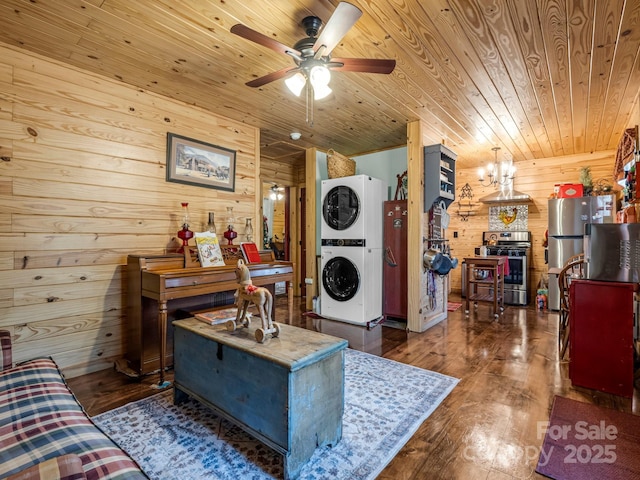 living room featuring wooden ceiling, dark hardwood / wood-style floors, stacked washer / dryer, wooden walls, and ceiling fan with notable chandelier