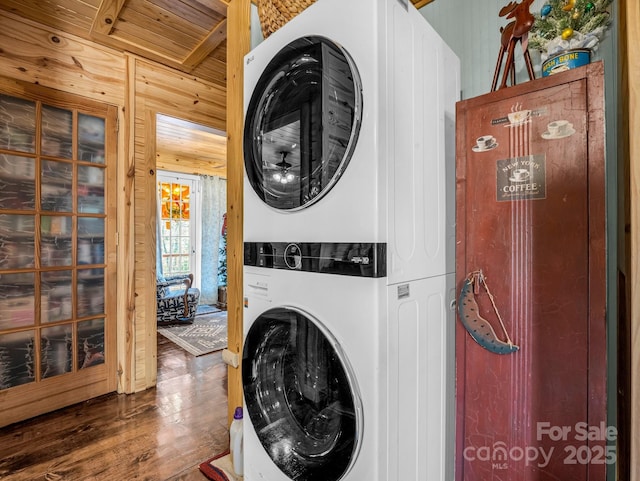 laundry room with dark wood-type flooring, stacked washing maching and dryer, and wooden walls