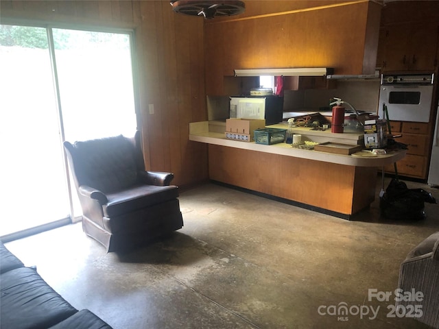 kitchen featuring concrete flooring, kitchen peninsula, oven, and wooden walls