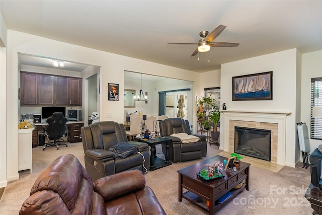 living room with a tiled fireplace, light colored carpet, built in desk, and ceiling fan with notable chandelier