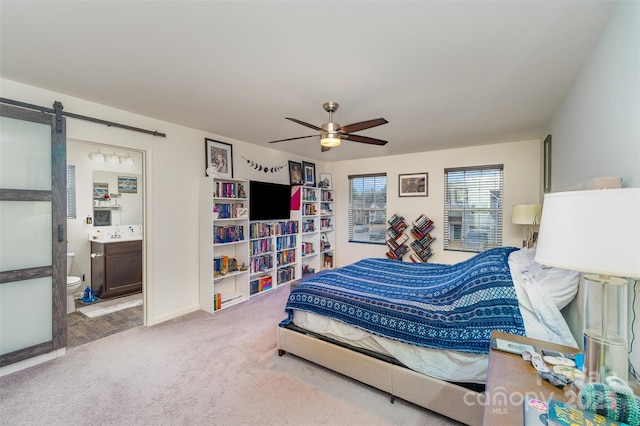 carpeted bedroom with connected bathroom, ceiling fan, and a barn door