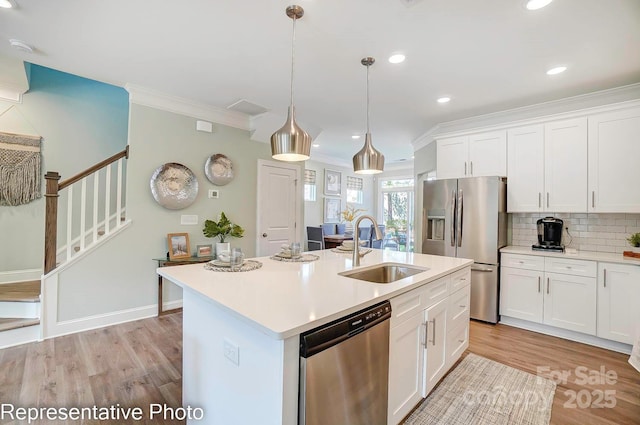 kitchen with stainless steel appliances, a kitchen island with sink, sink, pendant lighting, and white cabinets