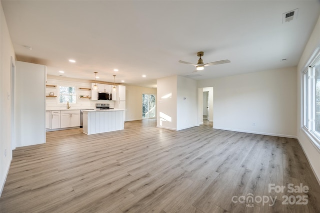 unfurnished living room with ceiling fan, plenty of natural light, sink, and light hardwood / wood-style flooring