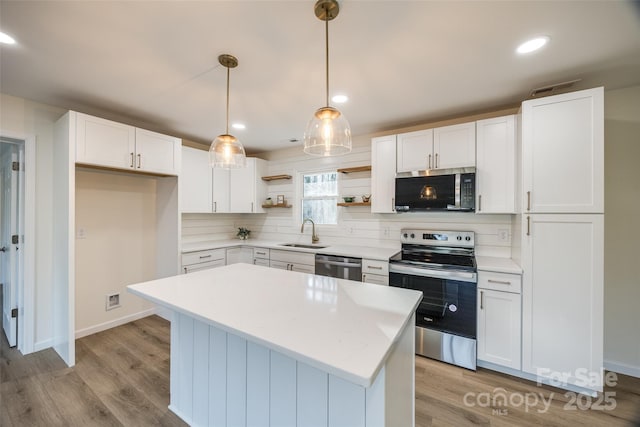 kitchen featuring a center island, sink, hanging light fixtures, white cabinetry, and stainless steel appliances