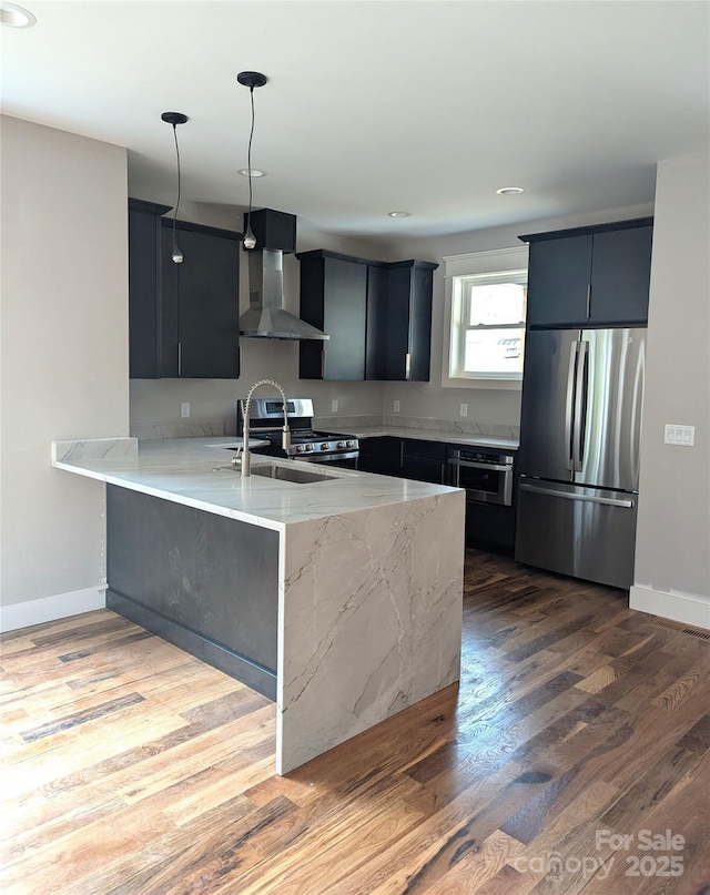 kitchen with wall chimney range hood, light stone countertops, a peninsula, wood finished floors, and stainless steel appliances