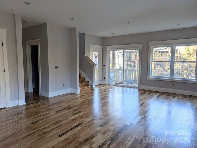 unfurnished living room with plenty of natural light, wood finished floors, and stairs