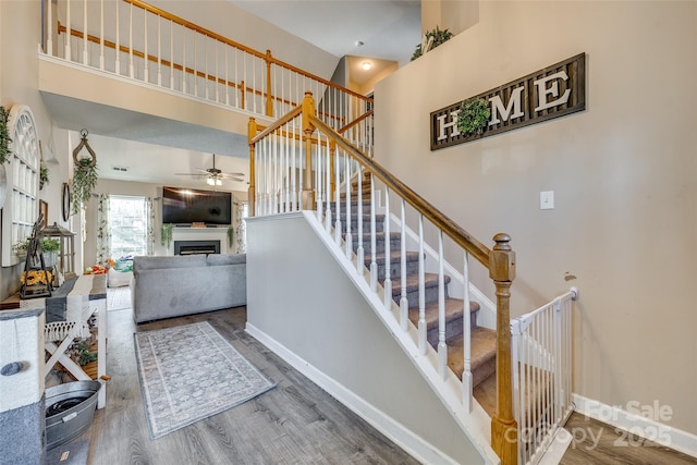 stairs with ceiling fan, hardwood / wood-style floors, and a towering ceiling