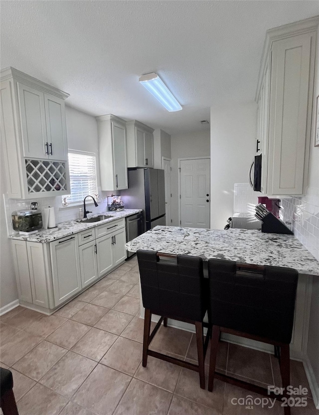 kitchen featuring appliances with stainless steel finishes, light stone countertops, light tile patterned floors, sink, and white cabinetry