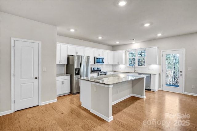 kitchen with backsplash, appliances with stainless steel finishes, a kitchen island, light stone counters, and white cabinetry