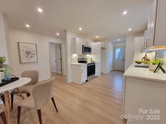 kitchen featuring sink, light hardwood / wood-style flooring, decorative backsplash, white cabinetry, and stainless steel appliances